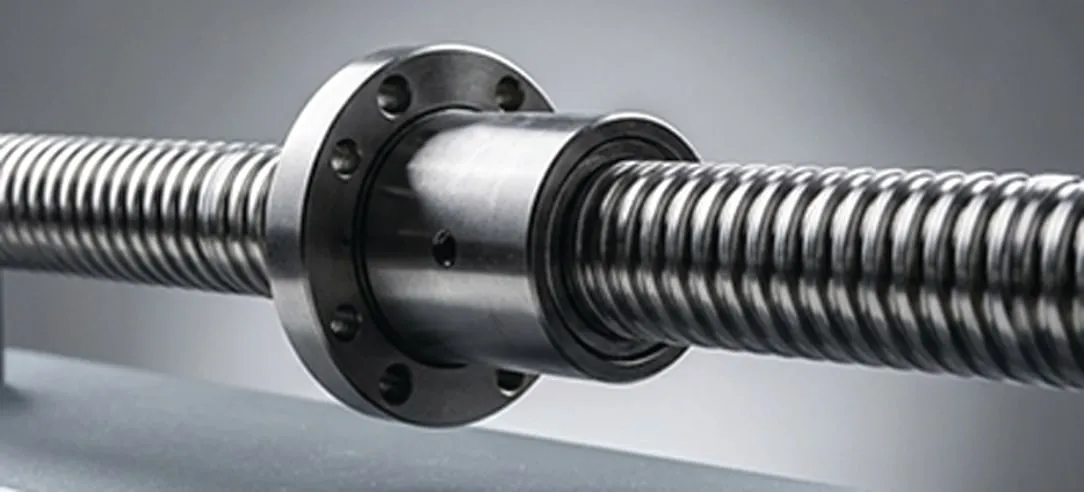 Close-up of a ball screw nut on its shaft, showing the bolt circle on the mounting flange, the seal at the nut face, and the ground helical raceway running out to either side.