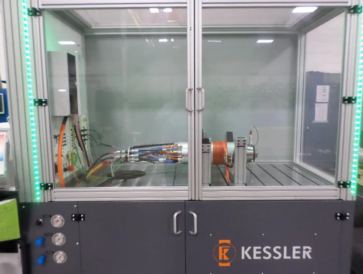 A Kessler Smart Test Stand: a glass-walled enclosure with a motorized spindle mounted on the bed, instrumented with coolant lines and sensor cabling.